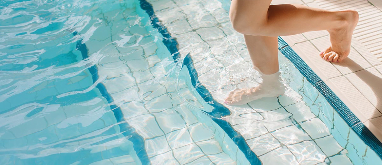 Feet entering a blue tiled swimming pool. Refreshing, summer, water fun.