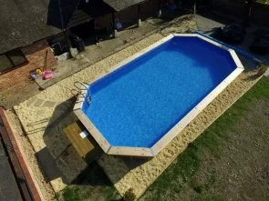 Above ground swimming pool with blue liner, wooden border, and ladder for backyard relaxation.