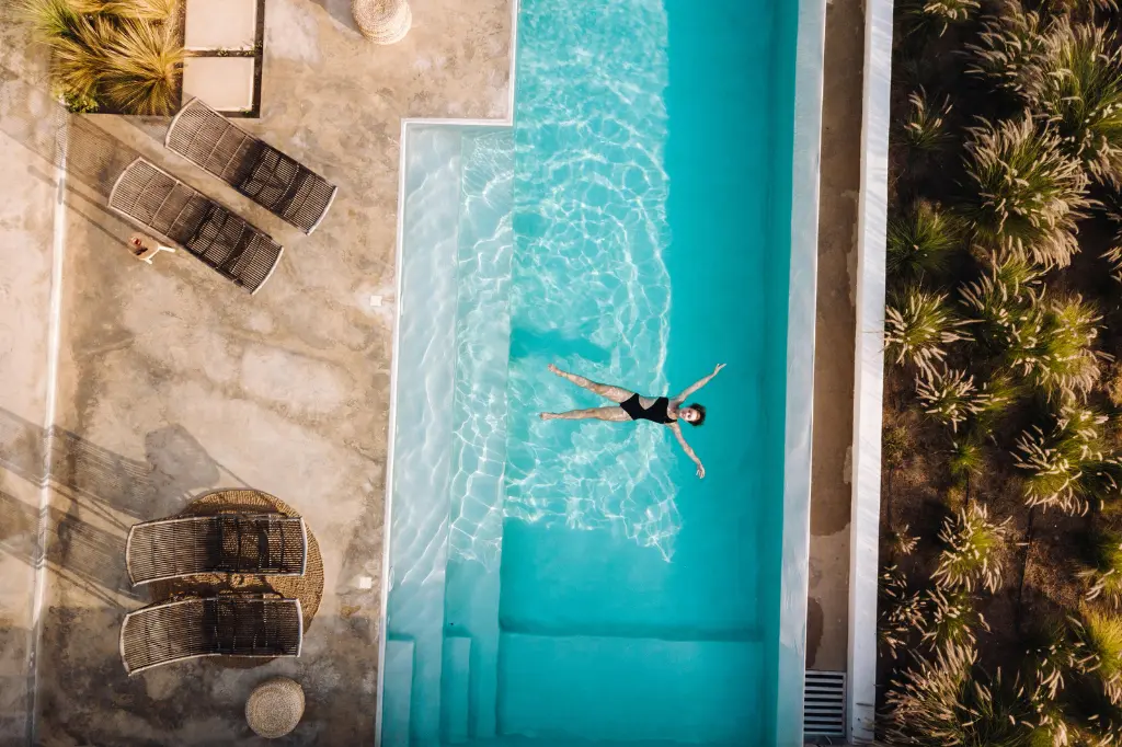 Lounge chairs by a turquoise pool, person swimming, outdoor relaxation.