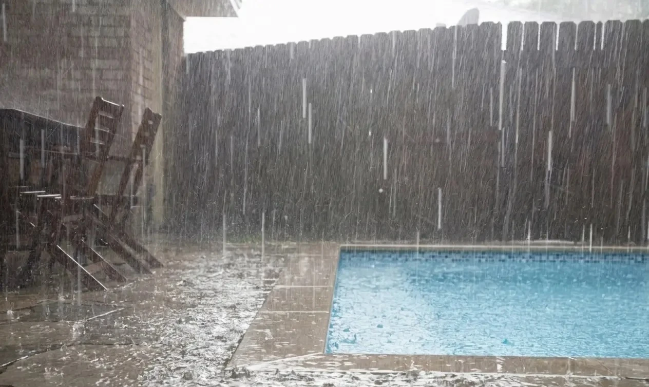 Swimming pool in the rain, blue water, wooden fence, stone patio, outdoor relaxation.