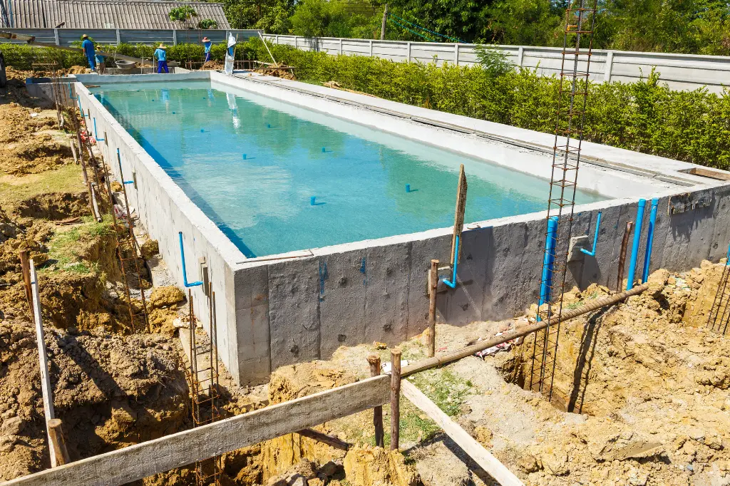 Concrete swimming pool under construction with blue water. Blue pipes and steel rebar. Building a concrete pool.