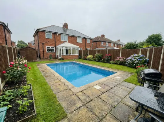 Backyard swimming pool with blue water and stone patio, perfect for outdoor recreation and relaxation.